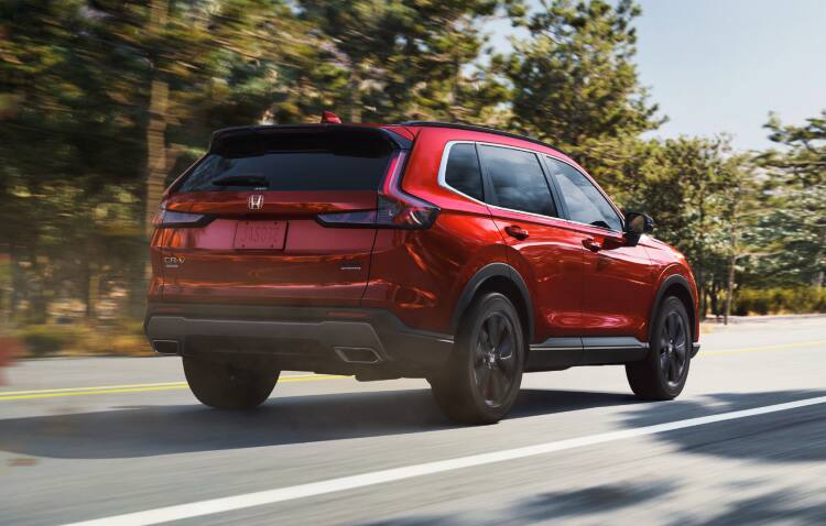Vista de perfil desde el lado del pasajero de la Honda CR-V Touring 2022 en Sonic Gray Pearl, conduciendo por un entorno urbano de noche.